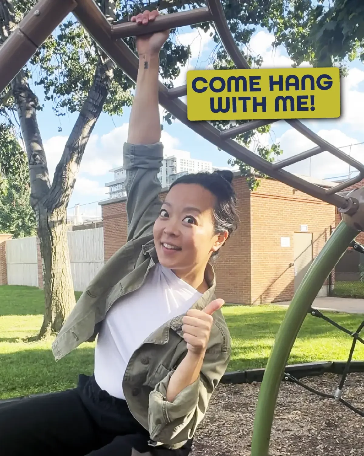 Fran Hong smiling and giving a thumbs-up while hanging from jungle gym with one arm, wearing a light jacket and white shirt, with the text ‘Come hang with me!’ displayed in a yellow box beside her.