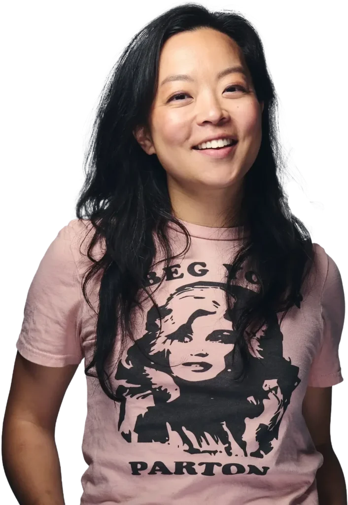 Fran Hong with long black hair smiling, wearing a pink T-shirt with a graphic of a Dolly Parton and the text "BEG YOU PARTON".